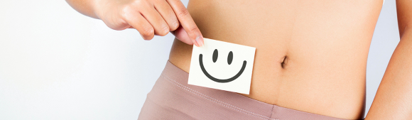 Person holding a smiley card in front of their abdomen, representing digestive health, gut wellbeing and the benefits of fibre-rich nutrition.