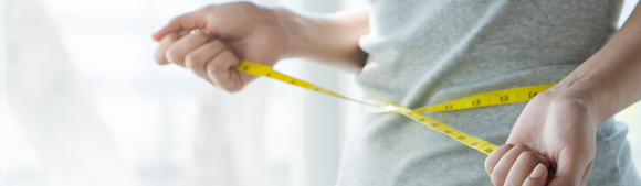 Person measuring waist with a yellow tape measure, representing weight management, healthy lifestyle, and body weight monitoring