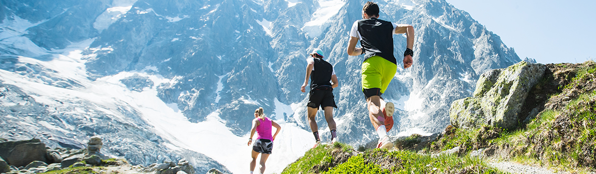 Three trail runners ascending a mountain path in a high-alpine landscape, highlighting endurance sports, outdoor performance and sustained energy during challenging terrain.