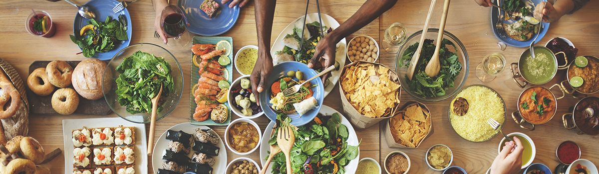 People sharing a variety of foods and beverages around a dining table during a social meal occasion.