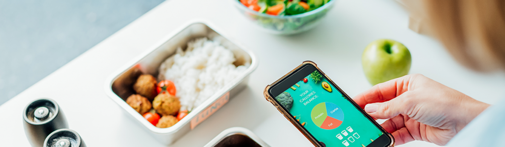 Person using a mobile nutrition tracking app while reviewing a balanced meal, illustrating personalized nutrition and healthy eating habits.