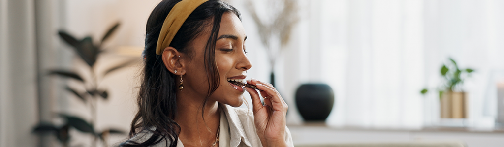 Woman enjoying a piece of chocolate in a relaxed home setting, representing mindful indulgence and emotional wellbeing.