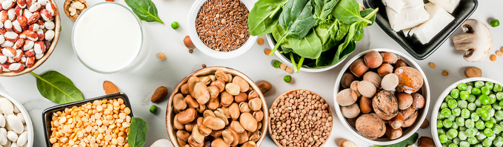 Assortment of plant-based protein sources including legumes, nuts, seeds, spinach, peas and tofu arranged on a table.